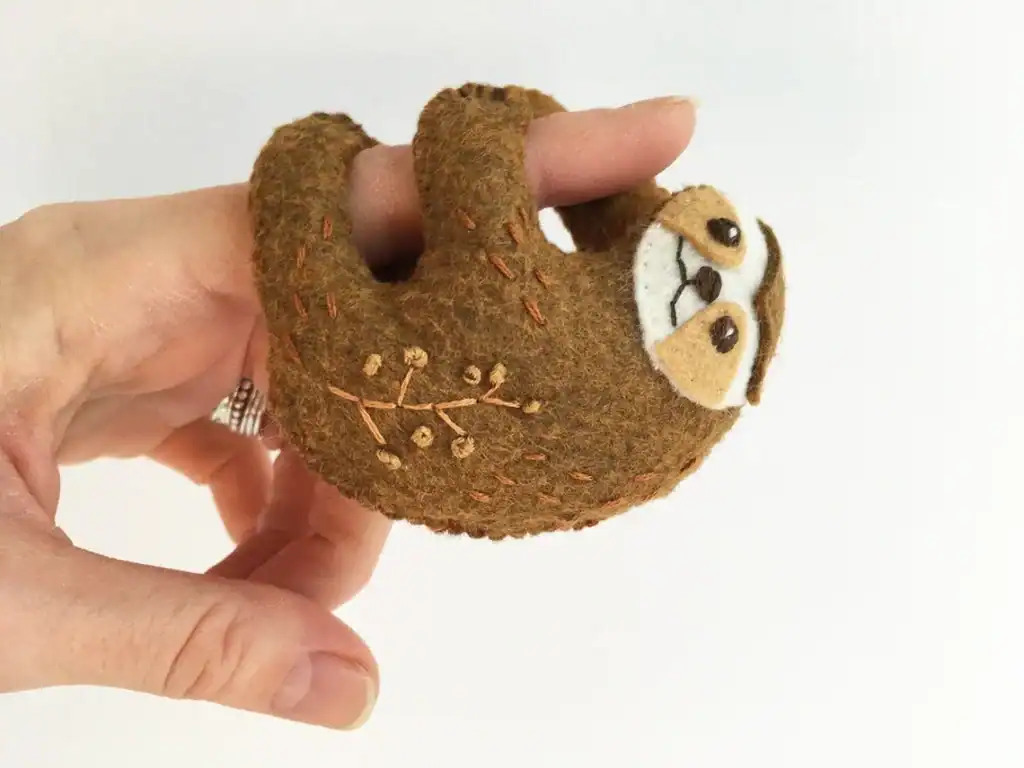 Felt sloth toy hanging from a finger