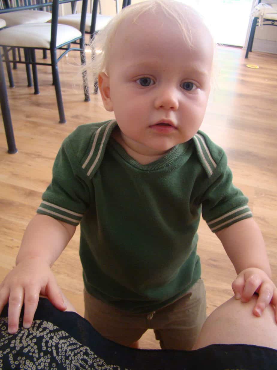 Toddler boy standing up wearing green envelope-neck Tshirt