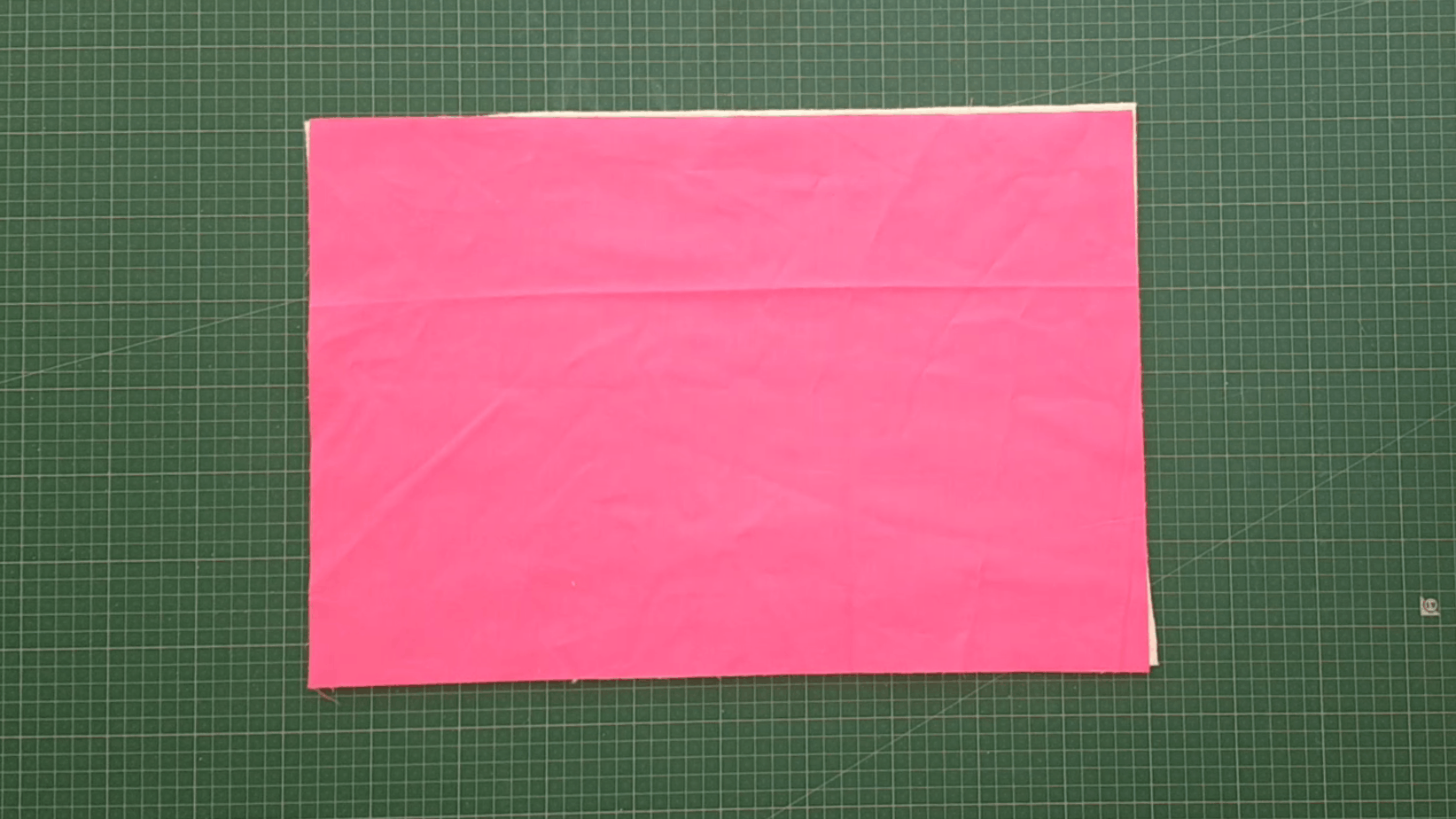 13" x 19" rectangle of pink fabric lying on top of the same size quilt batting on a cutting mat.