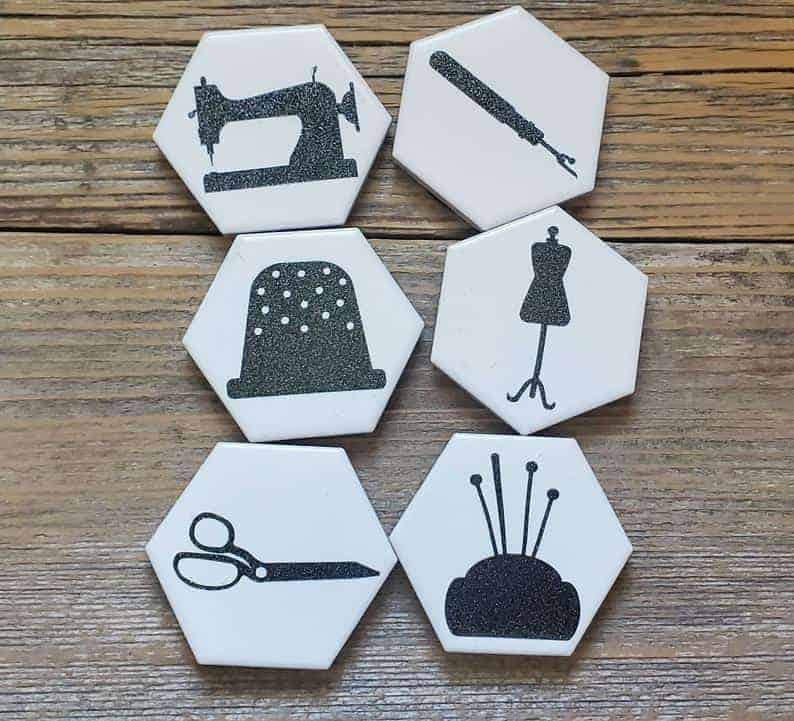 White hexagonal tiles with sewing notions pictures in black glitter paint, to be used as fabric weights