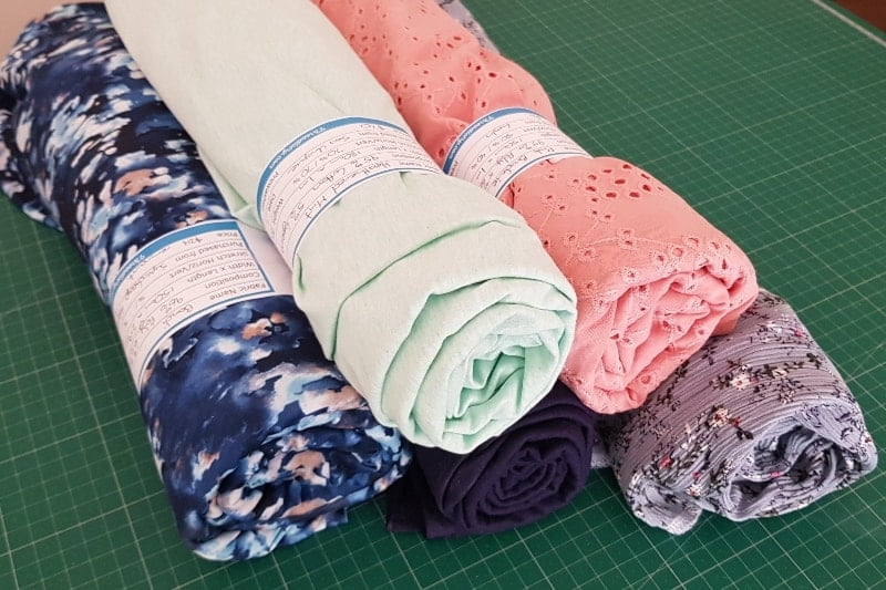 Rolls of fabric on a cutting mat, with fabric stash labels wrapped around them.