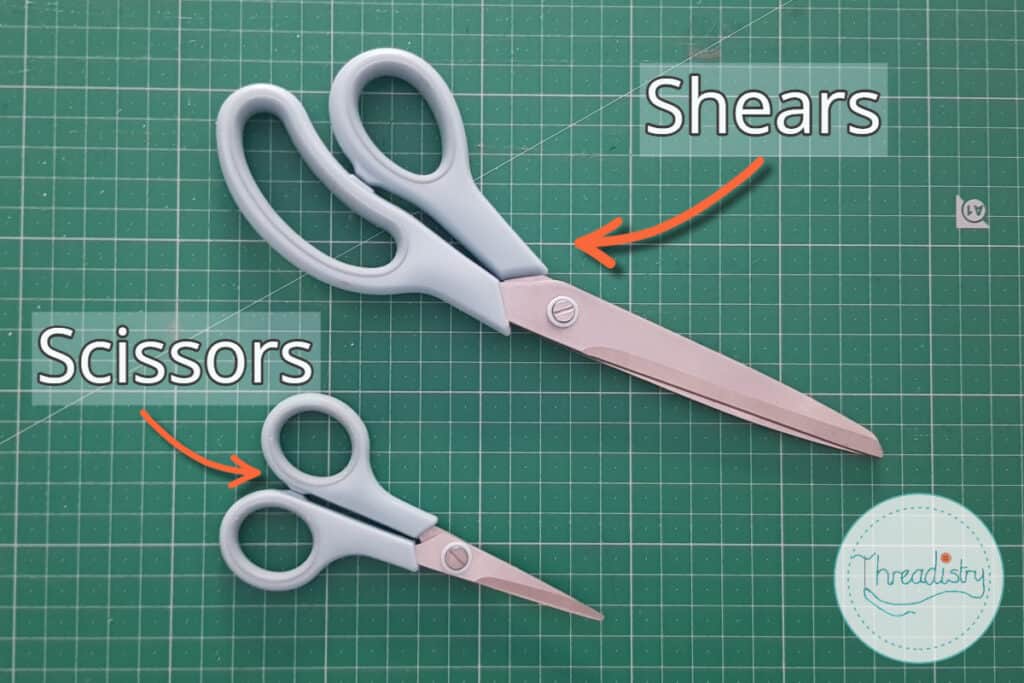 Fabric shears and sewing thread scissors lying on a green cutting mat.