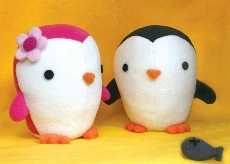 Two whimsical felt penguins, one pink and white with a flower and one balck and white.