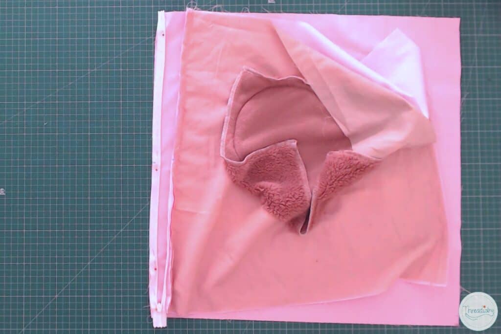 Second side of a zipper pinned in place on one edge of a pink square of fabric
