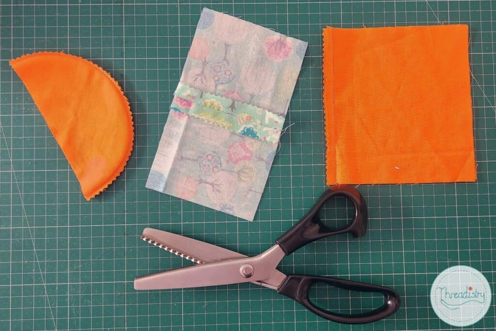 Pinking shears lying next next to 3 fabrics trimmed with pinking shears