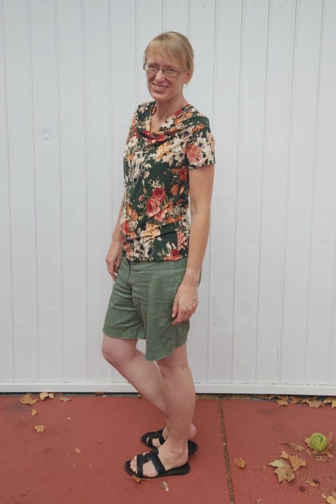 As side view of Narelle from Threadistry wearing a cowl neck top in a floral print with olive background.