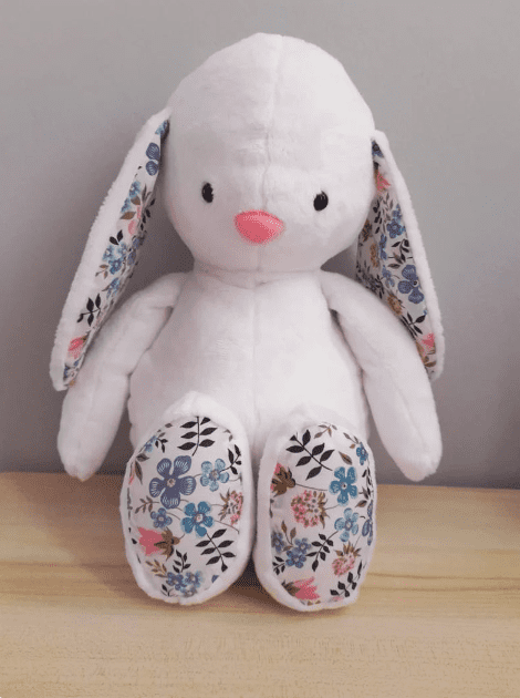 White plushie bunny with floral fabric on feet and in ears.