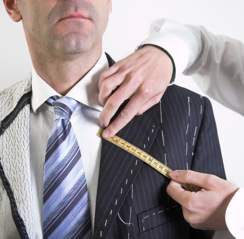 Tailor's hands taking measurements on an unfinished suit jacket