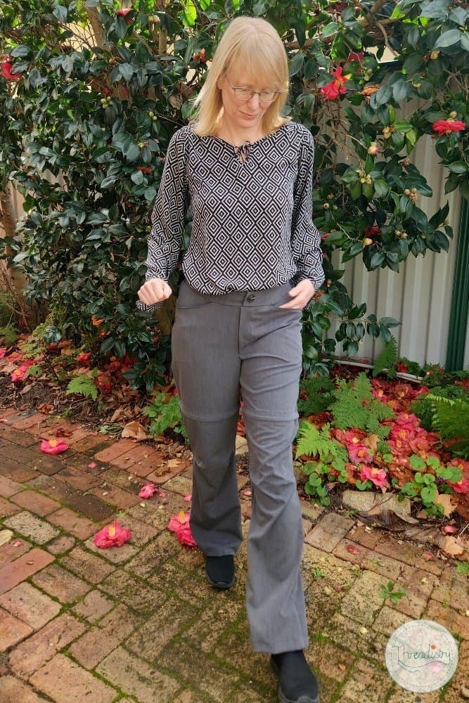 Elegant woman in stylish office wear walking outdoors among flowering plants.