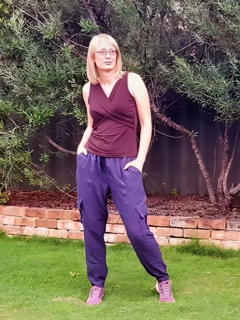 Comfortable casual woman outdoor fashion in garden with trees and brick border.