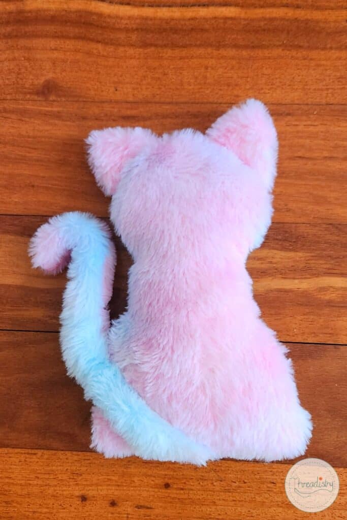 Fluffy pink and white plush cat toy on wooden surface.