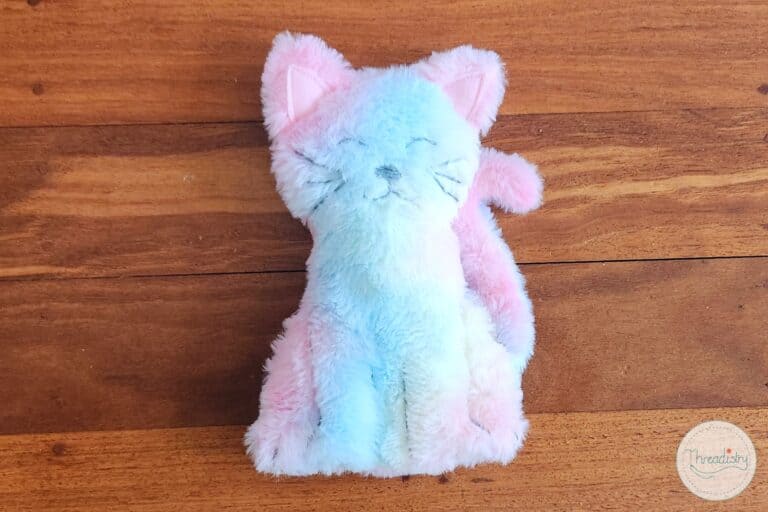 Soft pastel plush cat stuffed toy on wooden surface, kawaii cute animal pillow for kids and teens, cozy decorative plushie.