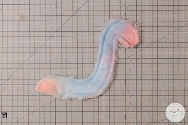 Soft pastel-colored fluffy yarn snake on gridded background for embroidery or craft projects.
