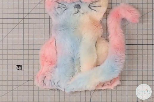 Fluffy pastel-colored cat-shaped embroidery hoop art on grid background.