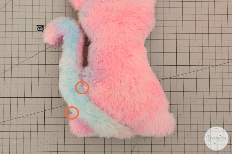 Colorful plush toy with soft furry texture, pink, blue, and white, on cutting mat background.