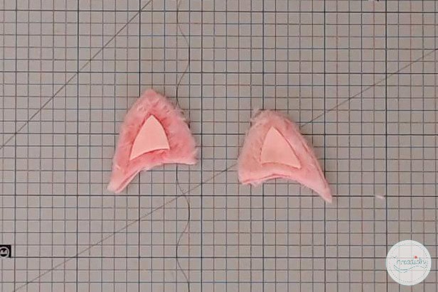 Faux cat ears made from pink fabric and faux fur on graph paper background.