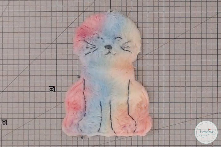 Fluffy pastel-colored cat embroidery on grid fabric, handcrafted textile art for home decor.