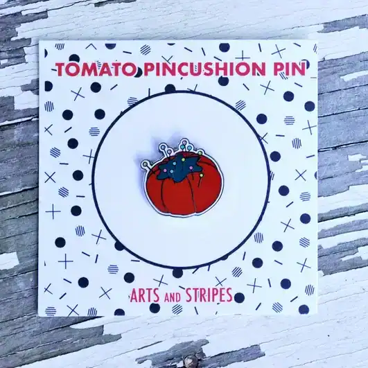 Colorful tomato pincushion pin with pins on a decorative card for sewing projects.