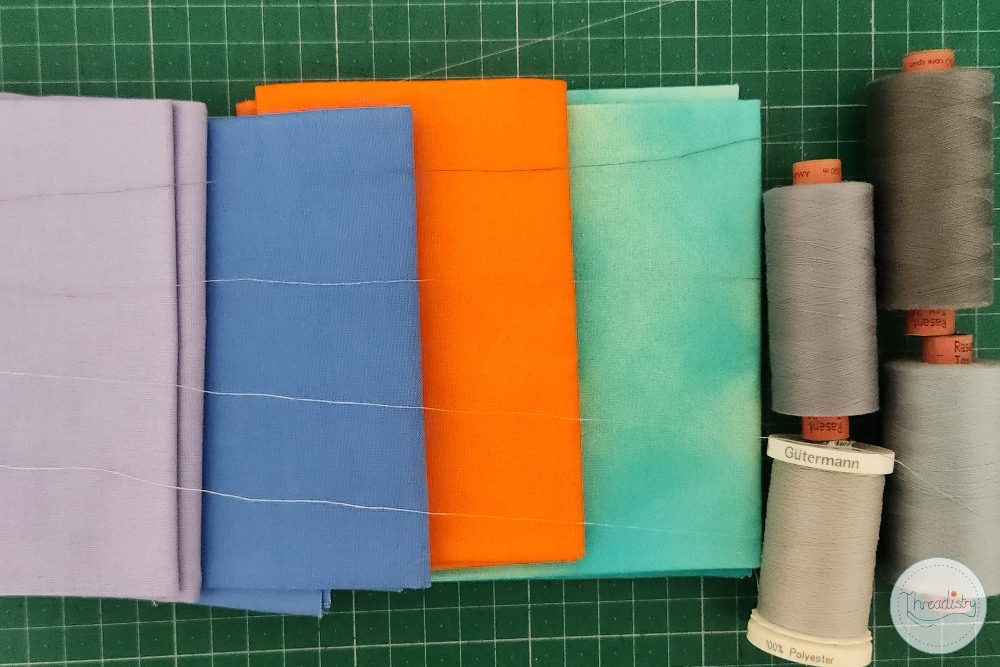 Colorful spools of thread on a green cutting mat for sewing projects.