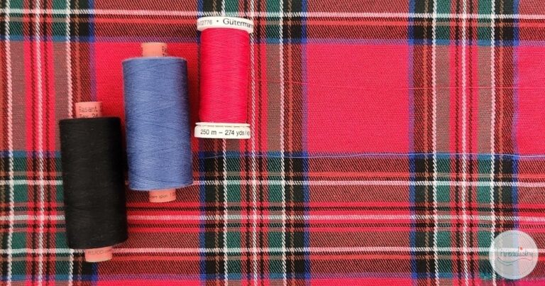 Colorful sewing threads on a red plaid fabric background.