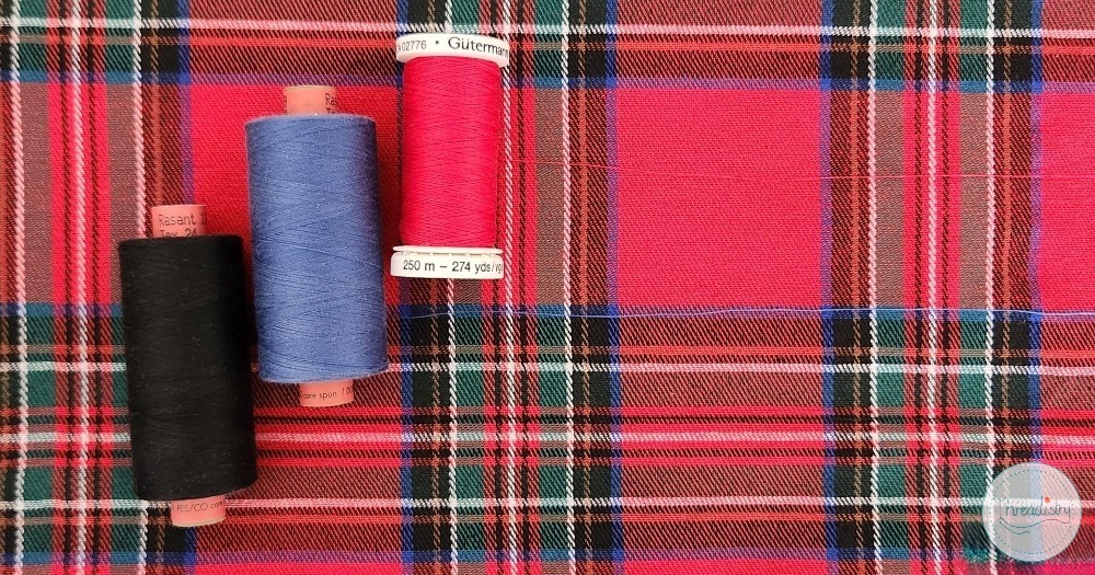 Colorful sewing threads on a red plaid fabric background.
