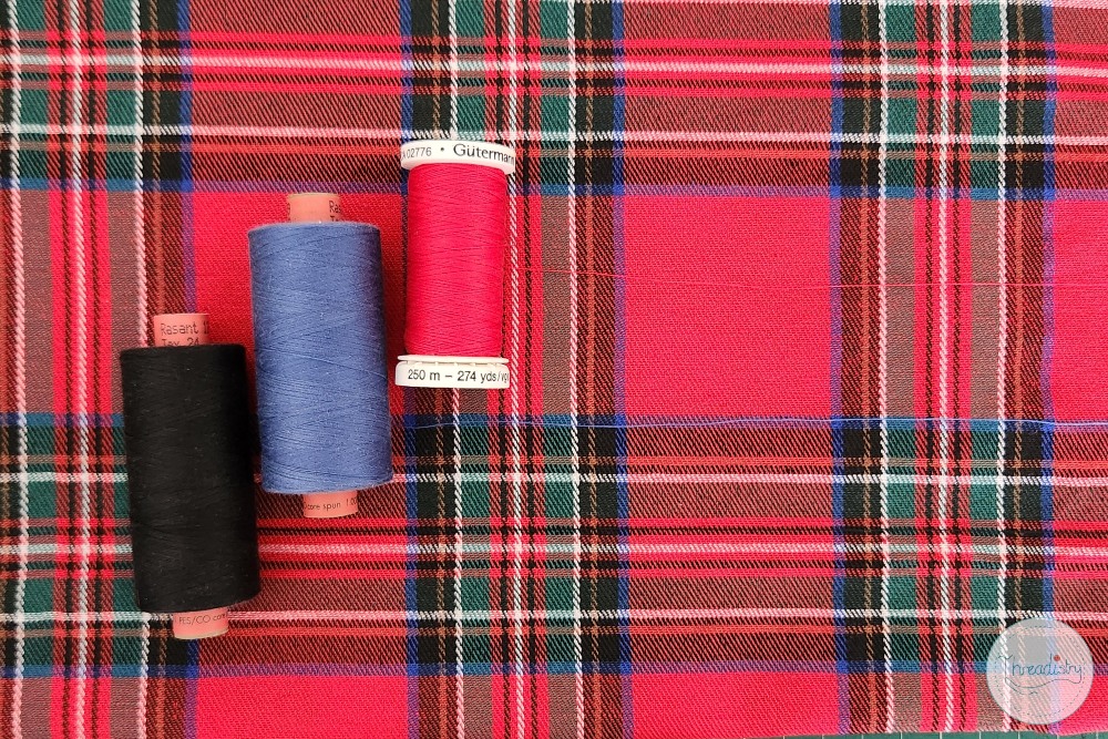 Colorful sewing threads on a red plaid fabric background.