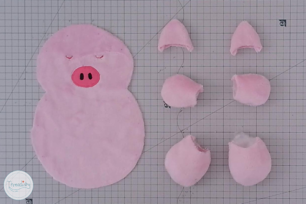 Pink piggy plush toy in progress with fabric pieces for assembly.