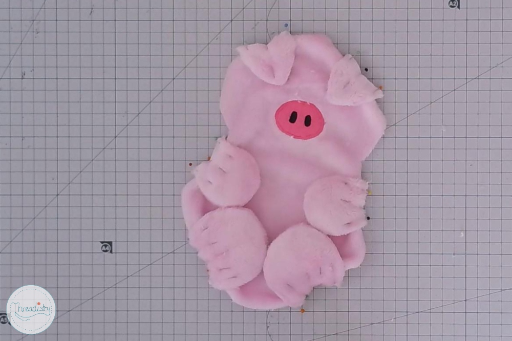 Pink plush piggy toy with a cute face and floppy ears on a grid background.
