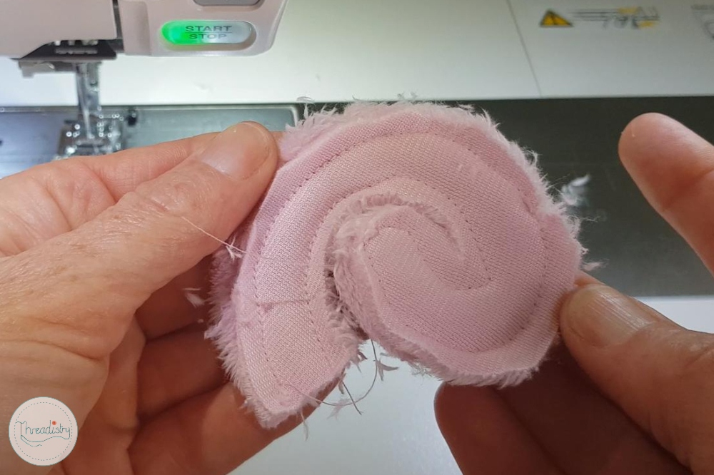 Pink fabric swirl with frayed edges, close-up of sewing process.