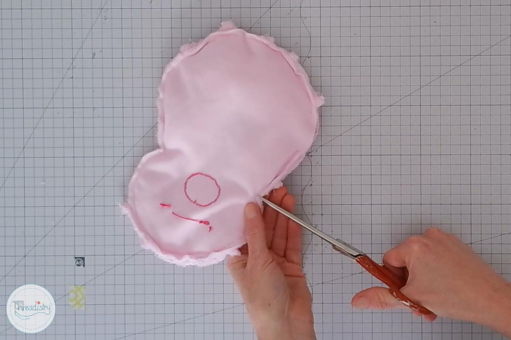 Sewing pink fabric to create a piggy bank with a circular face design.