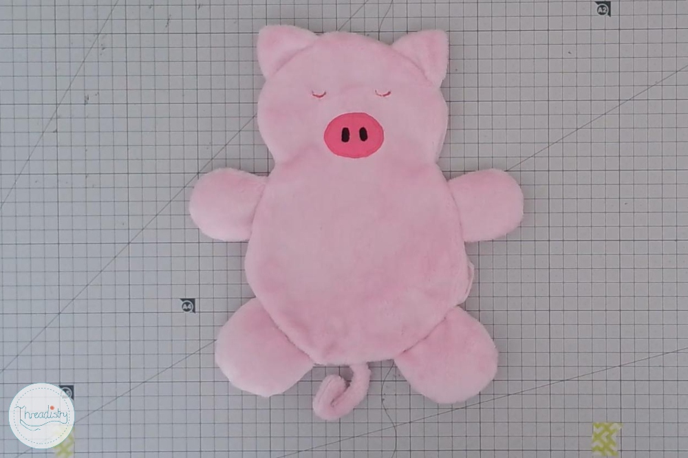Cute pink plush piggy toy with closed eyes and a curly tail on graph paper background.