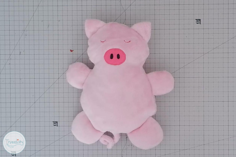 Cute pink pig plush toy with closed eyes on a grid background.