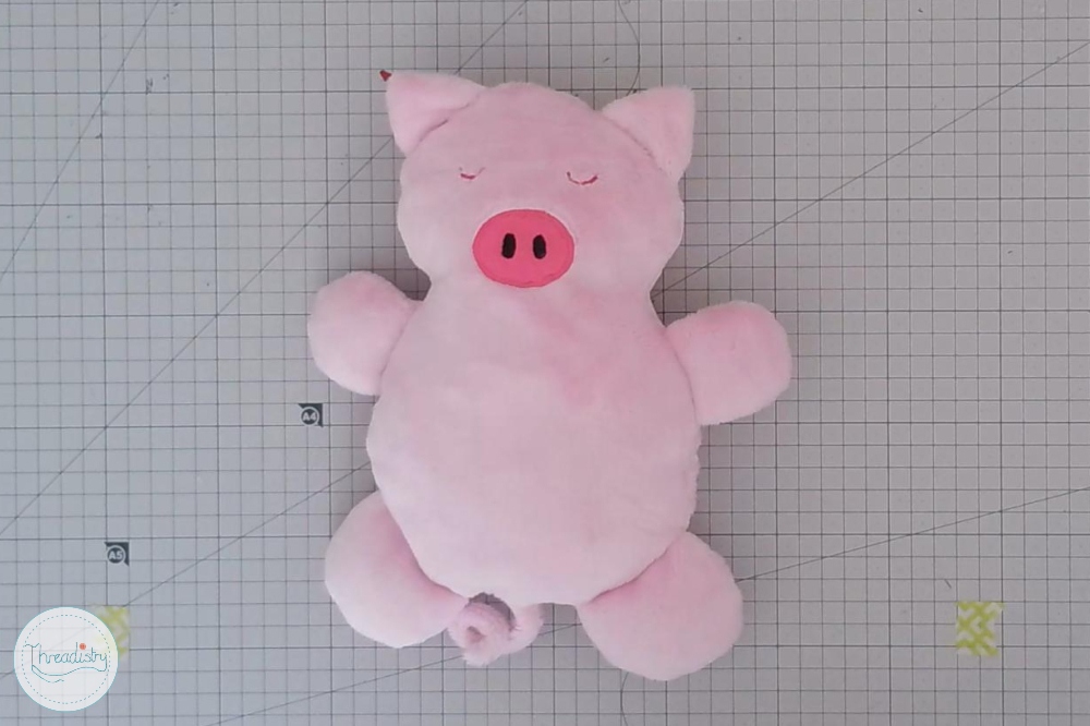 Cute pink plush pig toy with closed eyes on a grid background.