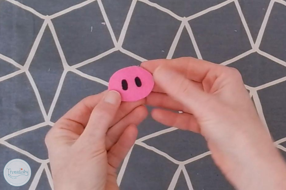 Pink piggy bank made from felt held by hands against geometric background.