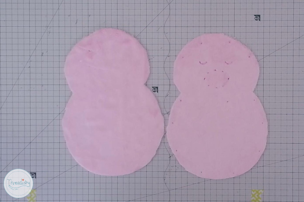 Pink fabric cutouts shaped like a snowman on graph paper background.