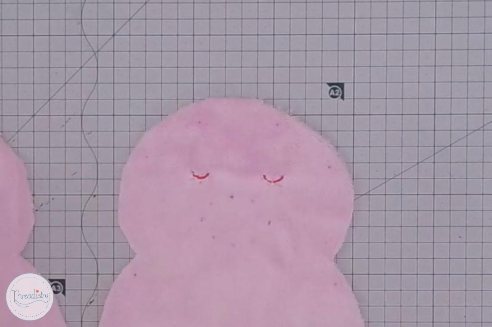 Pink plush piggy toy with closed eyes on graph paper background.