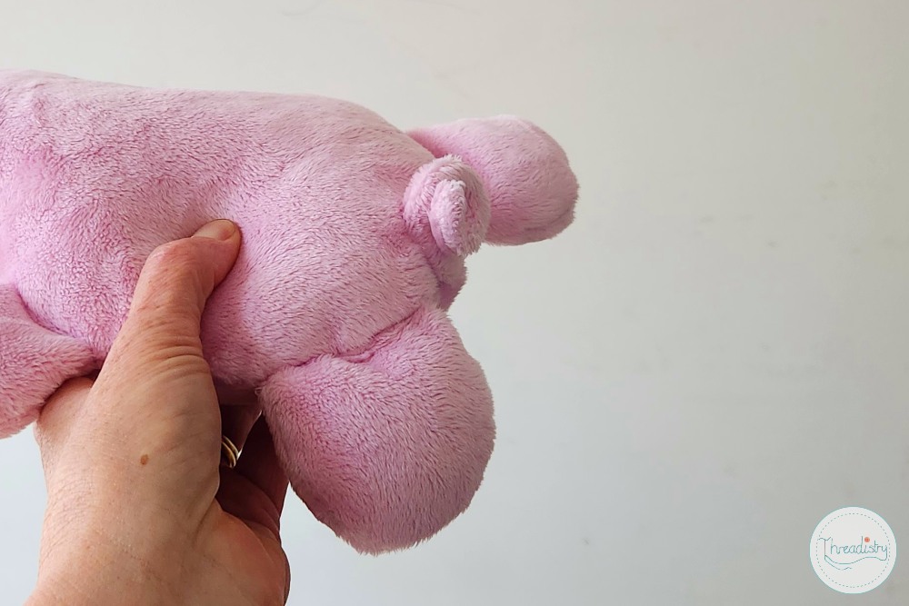 Pink plush piggy toy held in hand against a plain background.