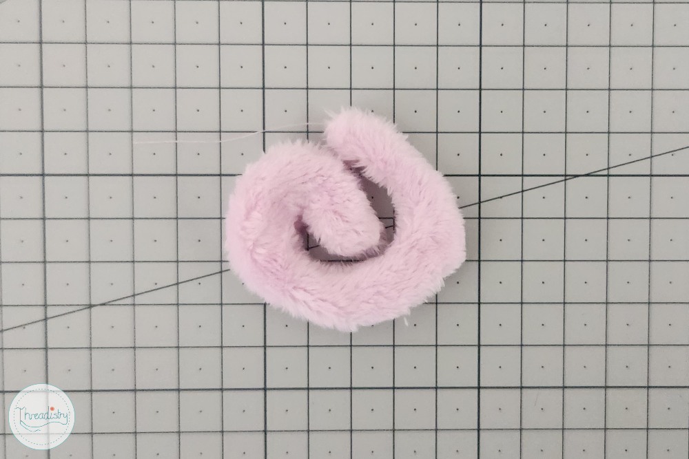 Soft pink plush hair tie on grid background, ideal for children's accessories.