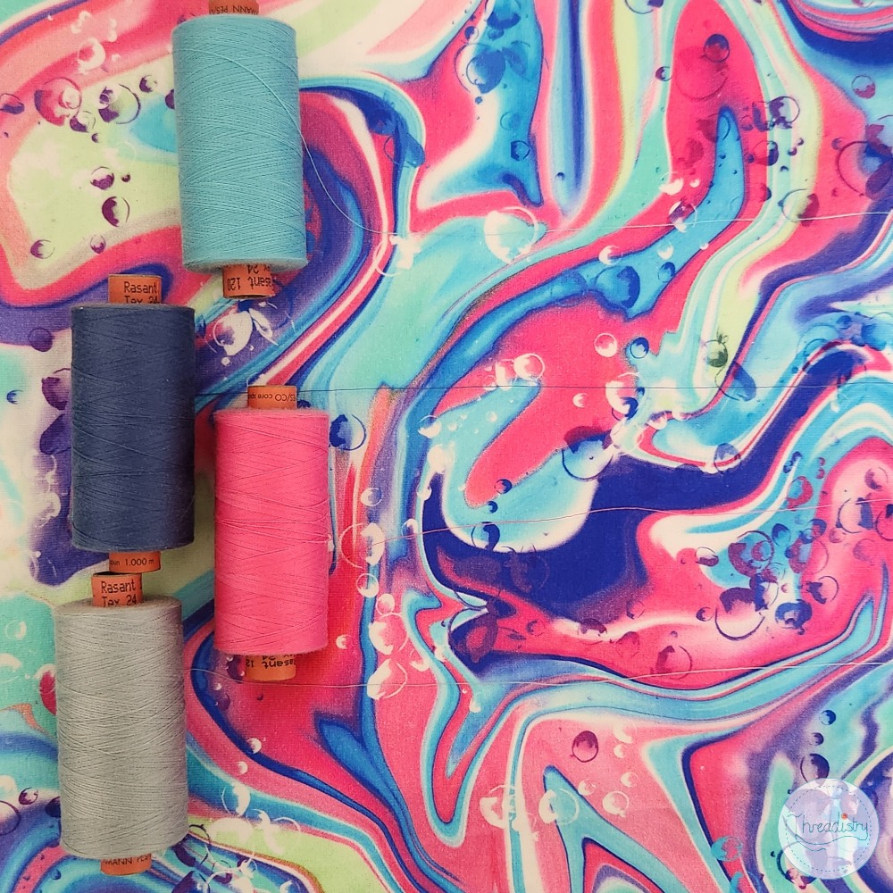 Colorful marbled fabric with spools of thread in blue, pink, and gray.