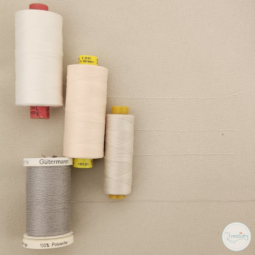 Spools of white, gray, and yellow thread on a beige background for sewing projects.