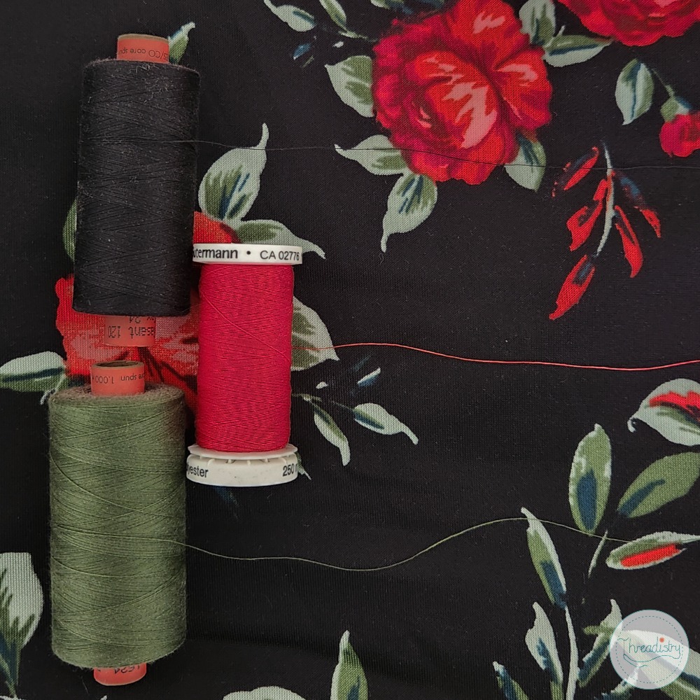 Colorful sewing threads on floral fabric background for quilting or sewing projects.