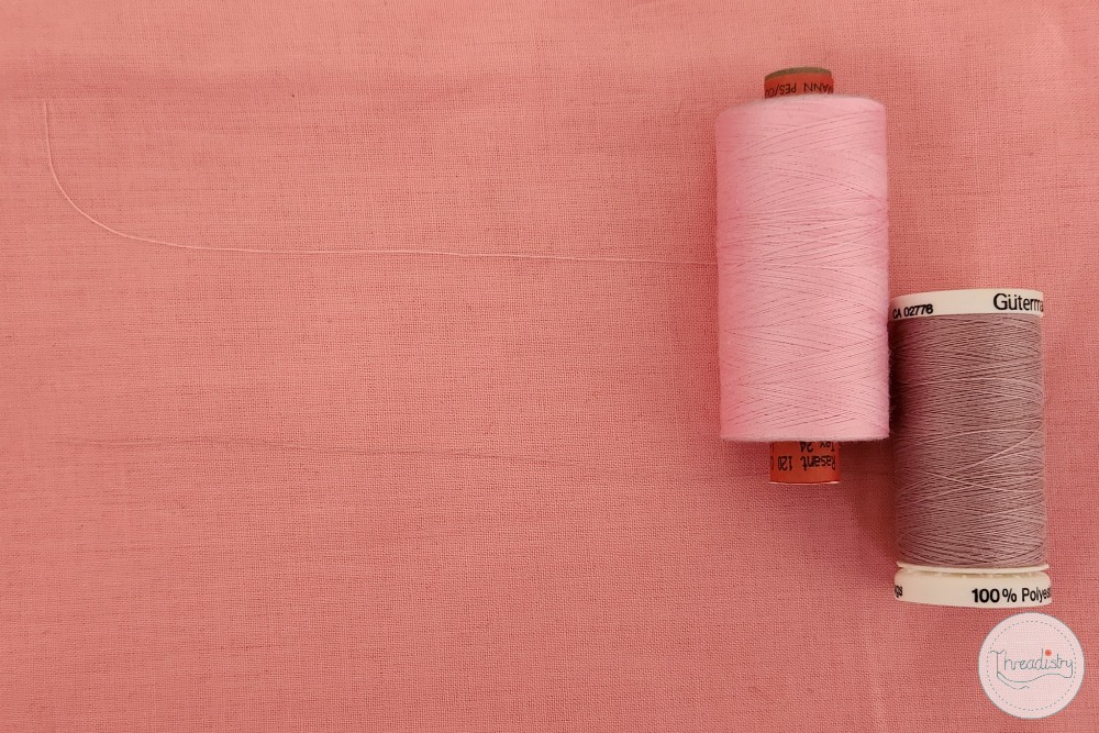Pink and gray thread spools on pink fabric background for sewing projects.